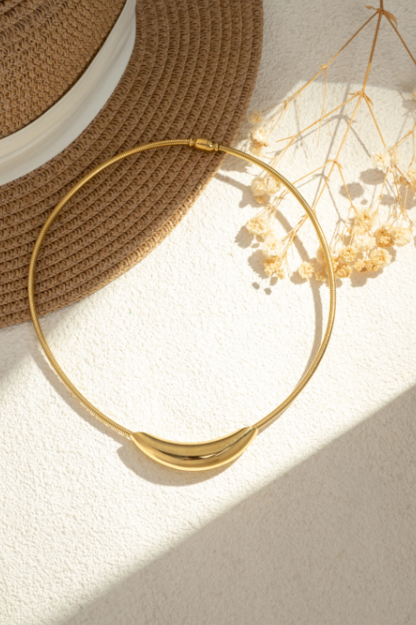 Collier Harmonia doré porté au cou avec pendentif courbe lisse et style minimaliste.