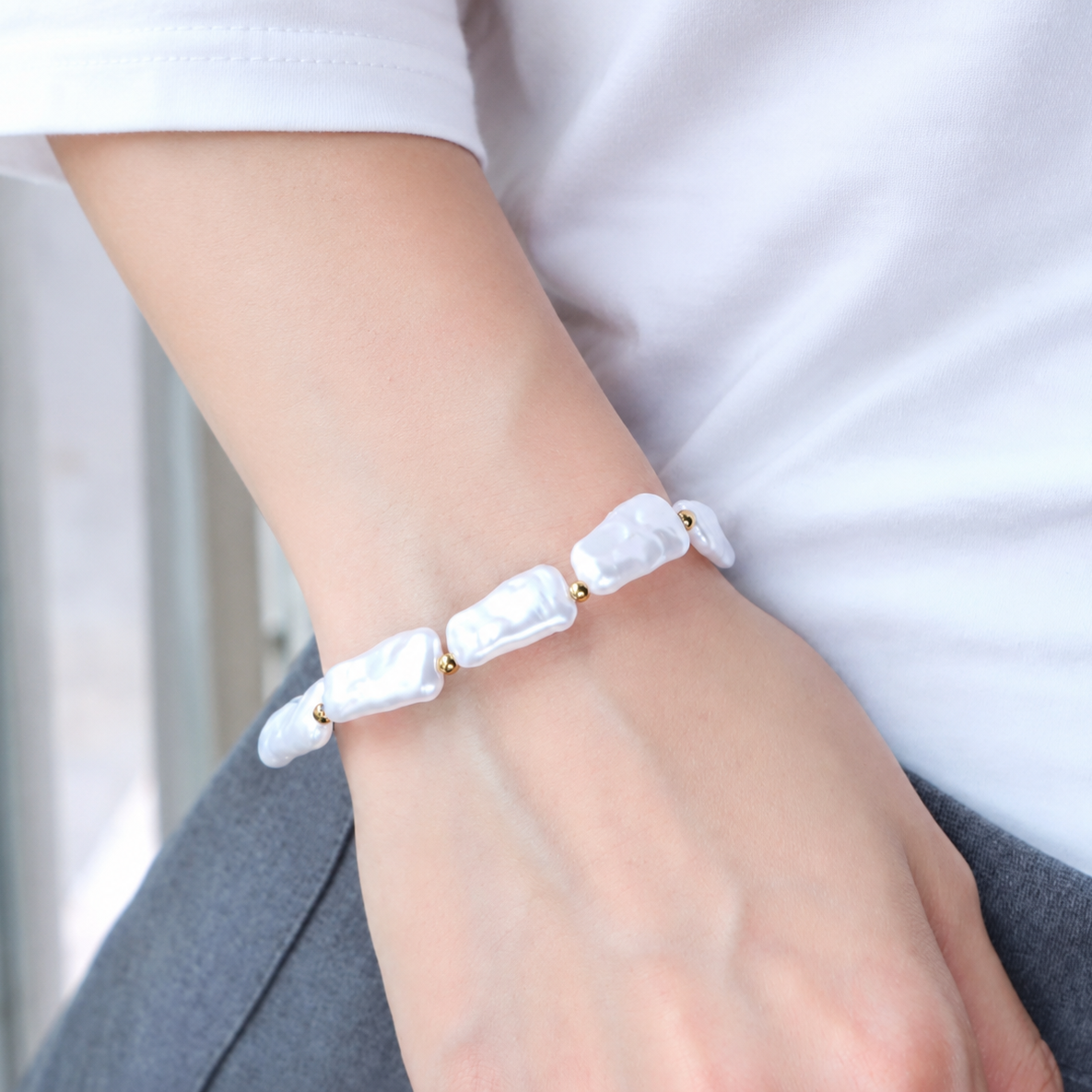 Bracelet Nausicaa avec perles blanches irrégulières et détails dorés porté au poignet.