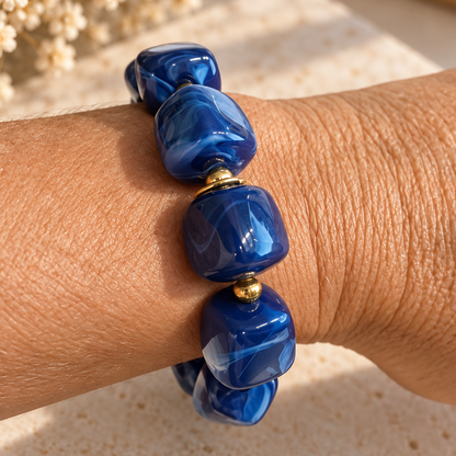 Bracelet AZURA porté au poignet avec grosses perles en résine bleu marbré et détails dorés