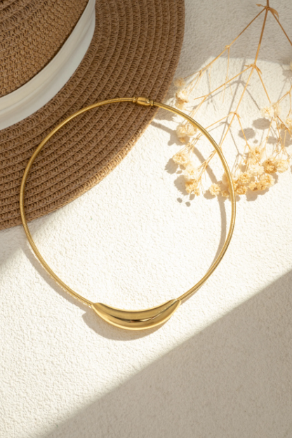 Collier Harmonia doré porté au cou avec pendentif courbe lisse et style minimaliste.